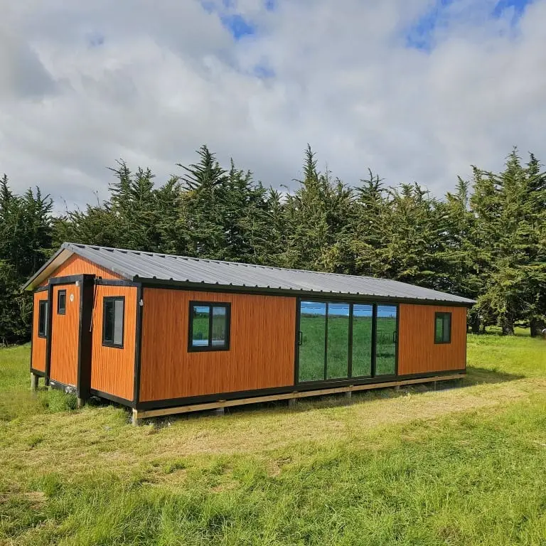 40 ft tiny home with cedar-look cladding and black joinery set on rural pasture in New Zealand